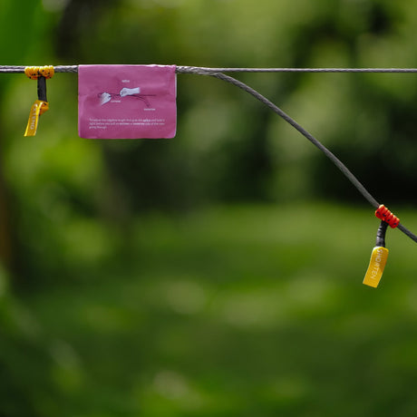 Ticket to the Moon Ridgeline Kit cord with yellow and red adjusters and a pink instruction panel, strung through a forest